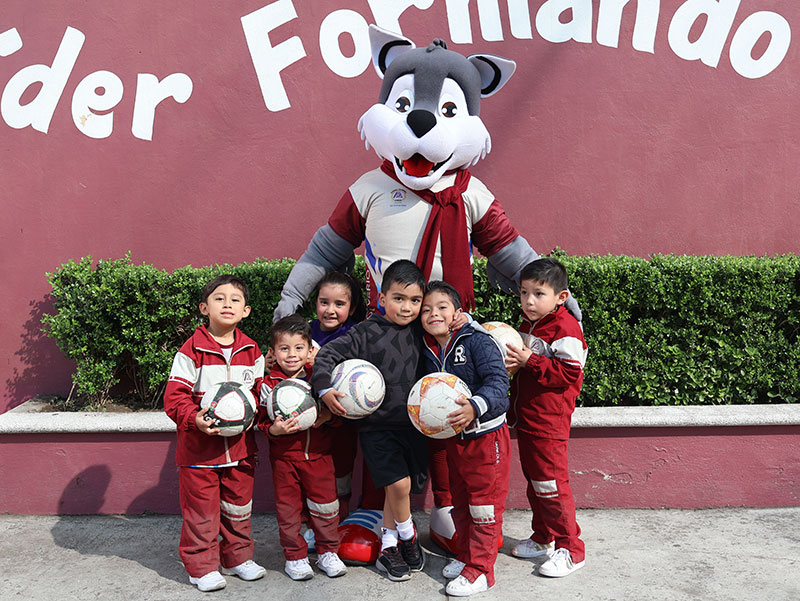 Grupo de estudiantes del Colegio Oliverio Cromwell en la clase de deportes con Lofito, la mascota del Colegio