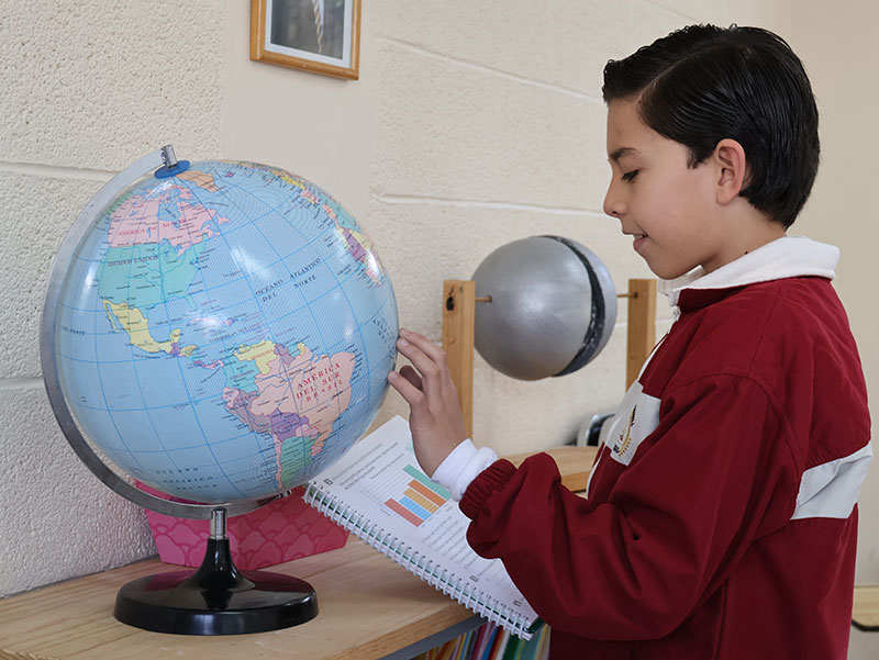 Estudiante de nivel primaria del Colegio Oliverio Cromwell estudiando con un globo terráqueo