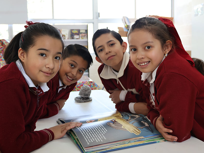 Estudiantes de nivel primaria del Colegio Oliverio Cromwell estudiando juntos con un libro